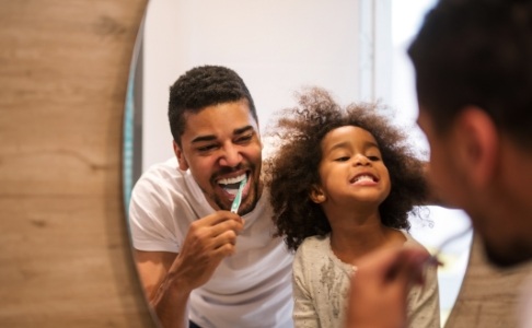 Father and daughter brushing teeth together to avoid dental emergencies