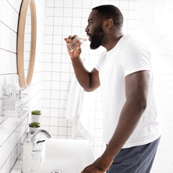 man brushing his teeth while looking in a bathroom mirror