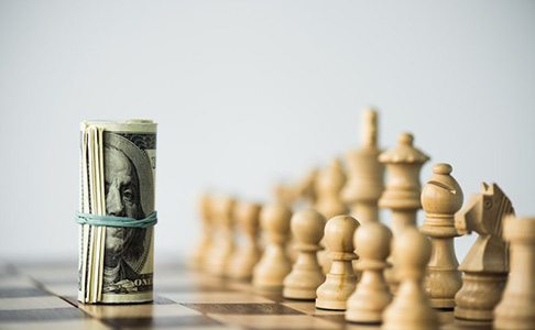 Rolled up wad of bills facing off against chess pieces on a chess board