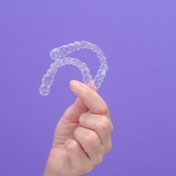Patient holding clear aligners against purple background