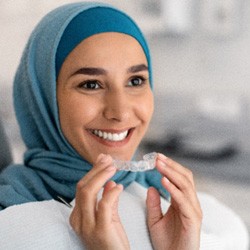 Woman smiling while holding Invisalign aligner in dental office