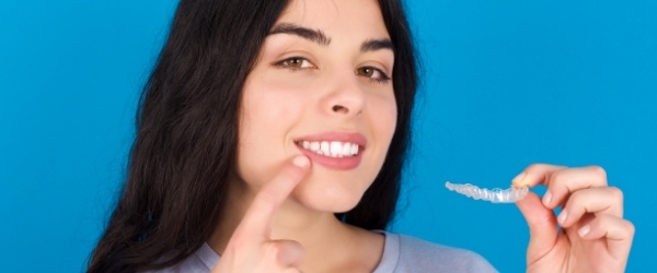 Woman pointing to smile and holding an Invisalign clear braces tray