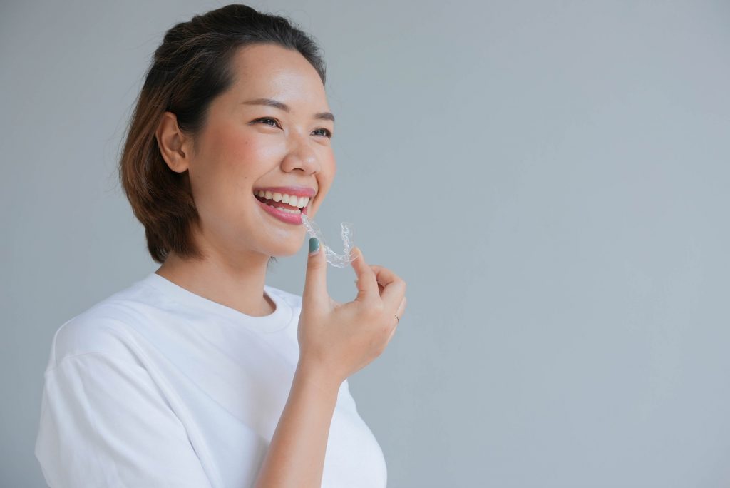 Woman in white shirt smiling while holding Invisalign aligner