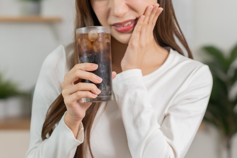 A woman touching her cheek after a cold drink triggers tooth sensitivity