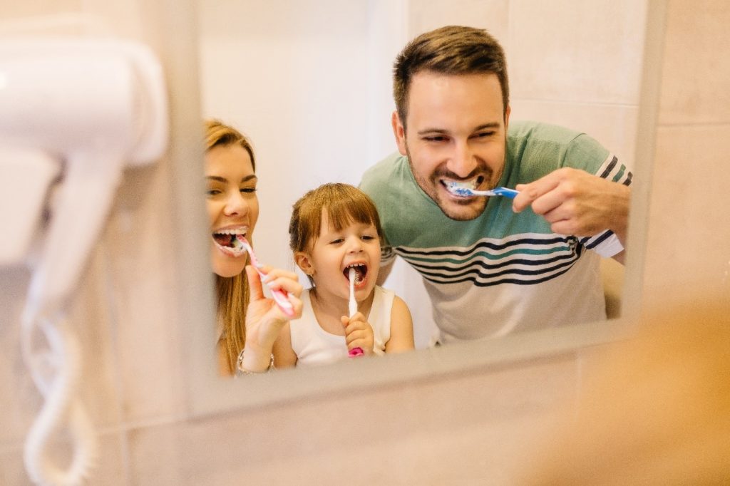 family smiling while brushing teeth together