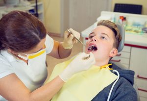 Teenager sitting in dental chair while a dentist examines their mouth