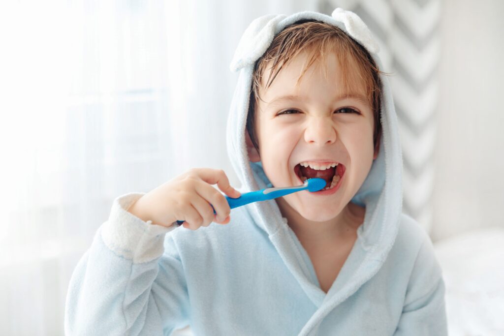 Little boy in hooded towel brushing his teeth